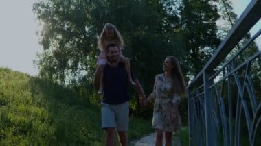 Güneşli bir yaz gününde parkta gezen bir çocuğu olan beyaz mutlu bir aile. Aile zamanı. Genç ve neşeli ebeveynler tatlı kızlarıyla yürüyüşe çıktılar. Ebeveyn tarzı. Mutluluk. Çocukluk konsepti. Gerçek