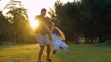 Young Caucasian male parent playing with little daughter on nature outdoors. Father holding child for hands spinning girl in park. Kid having fun with dad at sunset. Summertime. Family leisure concept