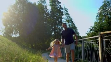 Genç mutlu ebeveynler ve kız doğada eğleniyor. Güzel, neşeli bir anne uçurtma uçururken babası küçük bir çocukla peşinden koşuyor. Gerçek zamanlı. Ailesi ve kızı parkta uçurtma oynuyorlar.