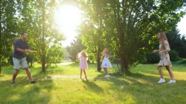 Happy cute family having fun weekend outdoors on nature. Wife and husband throwing frisbee disk in park while little children jumping cheering for parents. Summer outdoor activity. Family day concept