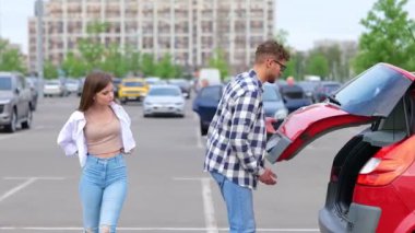 Genç bir adam ve bir kadın dışarıda park yerinde dururken bagajdan bavullarını çıkarıyorlar. Trip, ulaşım, ilişkiler, yaşam tarzı konsepti. Gerçek zamanlı.
