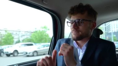 Taksi arabasının arka koltuğunda müzik dinlerken gülümseyen işadamı dans ediyor. İş, seyahat, ulaşım ve teknoloji konsepti. Gerçek zamanlı.