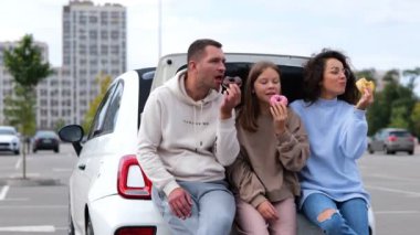 Beyaz, neşeli bir aile kadını ve elinde çöreklerle tezahürat yapan genç bir kızla gülümseyen bir adam. Gerçek zamanlı video. Genç kızı olan ebeveynler lezzetli çörekler yiyorlar. Çöreğin tadını çıkarıyorlar.