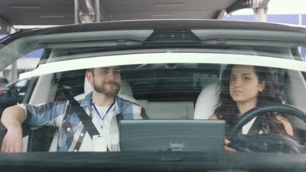 車を運転するために勉強している笑顔の女性 車の中で彼女の隣に座っている男性のインストラクター 運転テスト 輸送コンセプト スローモーション — ストック動画