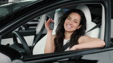 Gülümseyen güzel bayan sürücü koltuğunda otururken yeni arabanın anahtarını gösteriyor. Sürüş testi, ulaşım konsepti. Yavaş çekim