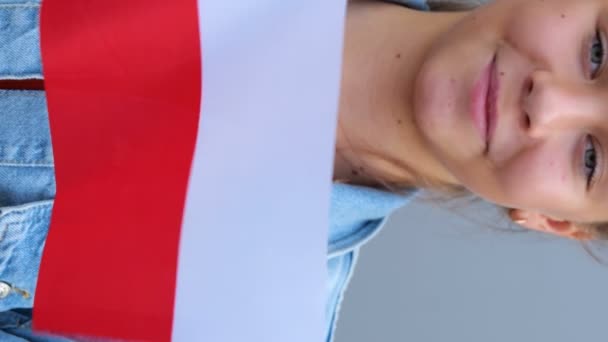 赤いTシャツとデニムのジャケットでポーランドの小さな旗を手にしたポーランドの十代の少女 若い女性は屋外に立って笑顔を浮かべ 小さなポーランド国旗を手で振っている リアルタイム — ストック動画