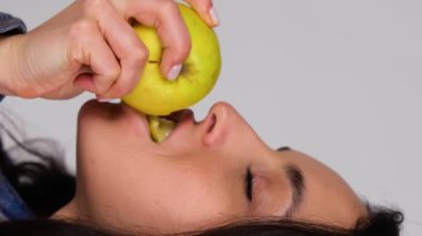 Gri arka planda izole edilmiş taze elma yiyen güzel genç bir kadın. Kopya alanı, yakın çekim. Sağlıklı, taze gıda konsepti. Gerçek zamanlı dikey video dikey video