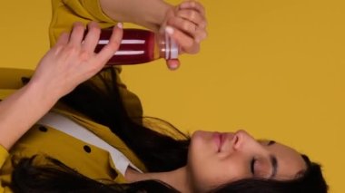 Mutlu kadın susuzluğunu gideriyor ve sarı arka planda izole edilmiş bir şişeden meyve suyu içiyor. Uzayı kopyala Yemek, yaşam tarzı konsepti. Gerçek zamanlı dikey video