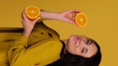 Mutlu kadın dans ederken eğleniyor, elinde narenciye dolu meyveler tutuyor. Sarı arka planda izole edilmiş. Diyet, insanlar ve ruh hali konsepti. Gerçek zamanlı dikey video