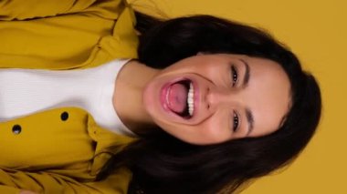 Gülümseyen genç bir bayan gözlerini kapatırken eğleniyor, turuncu bardakları sarı arka planda yapıyor. Diyet, insanlar ve ruh hali konsepti. Gerçek zamanlı dikey video