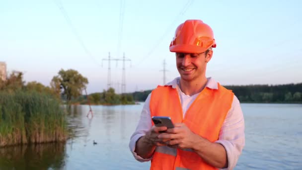 Uśmiechnięty Inżynier Elektryk Twardej Czapce Telefonu Komórkowego Najwyższe Napięcie Rzeka — Wideo stockowe