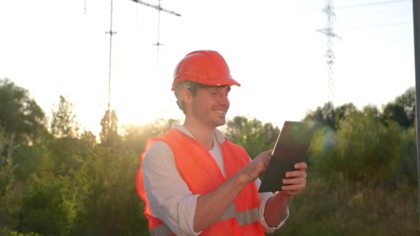 デジタルタブレットで作業しながら屋外に立っている笑顔の男性電気エンジニア 高圧パワーライン エネルギー産業コンセプト リアルタイム — ストック動画