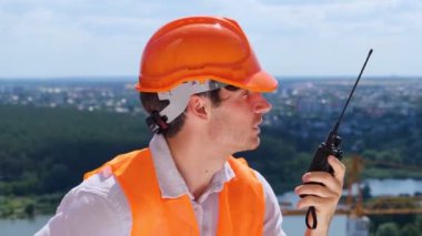 Erkek inşaat işçisi çatıda dikilirken telsizle konuşuyor. İş, inşaat, endüstri konsepti. Gerçek zamanlı.