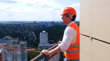 Şapkalı ve koruyucu gözlüklü gülümseyen erkek çalışanlar çatıda dikilip manzaranın tadını çıkarıyorlar. İş, inşaat, endüstri konsepti. Gerçek zamanlı.