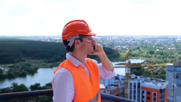 ヘルメットと保護眼鏡をかぶった男性ビルダーが 屋根の電話で話している ビジネス ビルディング 産業コンセプト リアルタイム — ストック動画