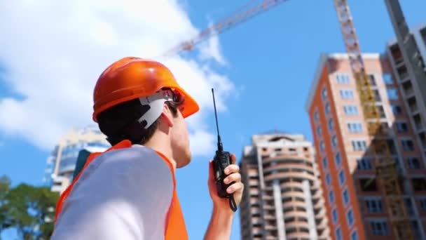 建物の近くに立っている建設現場で話しながら ウォルキー トーキーを使った男性ビルダー ビジネス ビルディング 産業コンセプト リアルタイム — ストック動画
