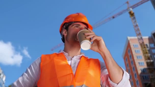ホットドリンクを飲んでいる間 建設現場に堅く立っている笑顔のビルダー ビジネス ビルディング 産業コンセプト リアルタイム — ストック動画