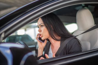 Genç iş kadını araba kullanıyor, cep telefonu kullanıyor, konuşuyor ve internette çalışıyor. Emniyet kemeri takan kadın. Ulaşım, iş, teknoloji, güvenlik kavramı