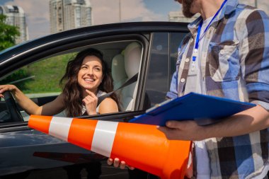 Dışarıda araba sürerken arabada oturan mutlu bayan, trafik konisi tutan erkek eğitmen. Test sürüşü, ulaşım, güvenlik, eğitim kavramı