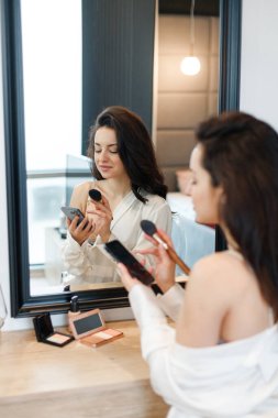 Genç bayan yatak odasında aynanın yanında otururken akıllı telefon kullanıyor. Seksi beyaz gömlek giyen bir kadın. Yaşam tarzı kavramı