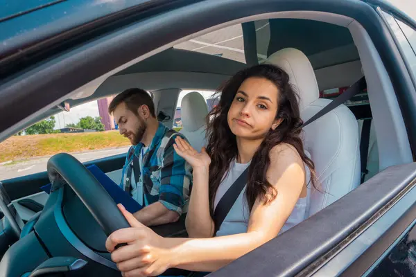 Disappointed lady driving the car during drive test while male instructor filling out notes in the report. Test drive, transportation, safety, education concept