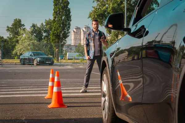 Erkek eğitmen ona yardım ederken, kız öğrenci dışarıda trafik konilerinin yanındaki parkta çalışıyor. Test sürüşü, ulaşım, güvenlik, eğitim kavramı