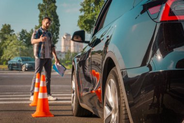 Sürücü kursunda sınav sırasında trafik konilerinin yanına park eden bir kadına yardım eden erkek eğitmen, açık havada duruyor. Test sürüşü, ulaşım, güvenlik, eğitim kavramı