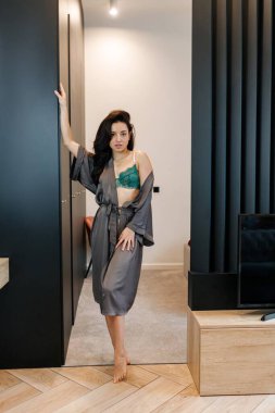 Evdeki odada sızlanırken gri gecelikle seksi iç çamaşırı giyen genç bir kadın. Romantik, tutkulu, yaşam tarzı konsepti.