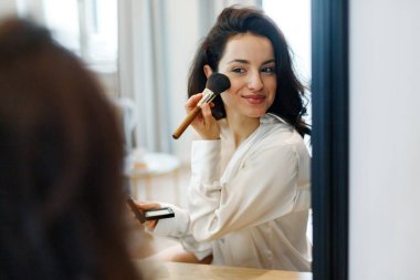 İç çamaşırlı güzel bayan aynaya bakıyor ve fırçayla kozmetik uyguluyor. Güzellik ve yüz estetiği, sabah rutin konsepti..