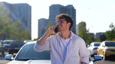 Şehirde cep telefonuyla konuşurken arabasının yanında duran gözlüklü gülen adam. Ulaşım, teknoloji ve yaşam tarzı konsepti. Yavaş çekim