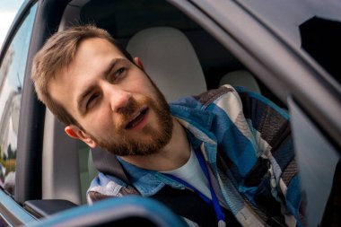 Yolculuğun tadını çıkaran mutlu genç erkek, arabanın camından dışarı bakarken yolcu koltuğunda oturuyor. Yolculuk, seyahat, yaşam tarzı konsepti