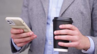 Genç adam cep telefonu tutuyor ve dışarıda kahvenin tadını çıkarırken daktilo yazıyor. İş, teknoloji kavramı. Yavaş çekim