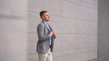 Gülümseyen genç adam ceketini düzeltiyor ve dışarıda yürüyor. Uzayı kopyala İş, iş kavramı. Yavaş çekim