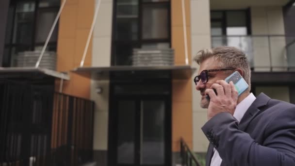 戴着眼镜的忙碌的商人一边走在大街上一边用智能手机交谈 技术概念 慢动作 — 图库视频影像