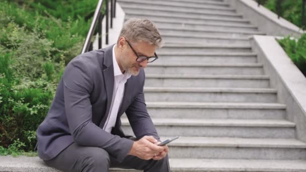 スマートフォンを持っているビジネスマンとステップの近くに屋外に座っている間タイピング ビジネス コミュニケーション 技術コンセプト スローモーション — ストック動画