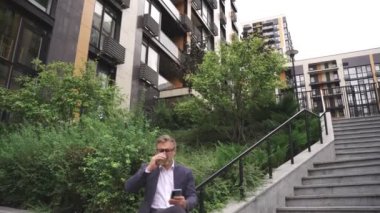 Kahve içerken ve dışarıdaki akıllı telefonda yazarken mutlu iş adamı oturuyor. İş, iletişim, teknoloji konsepti. Yavaş çekim