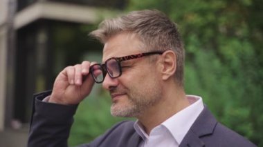 Gülümseyen işadamı sokakta durup gözlüğünü çıkarırken kameraya bakıyor. İş, insanların kavramı. Yavaş çekim