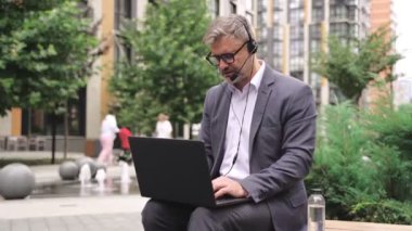 İş adamı kulaklık takıp internette konuşurken dizüstü bilgisayarda daktilo kullanıyor. İş, teknoloji kavramı. Yavaş çekim