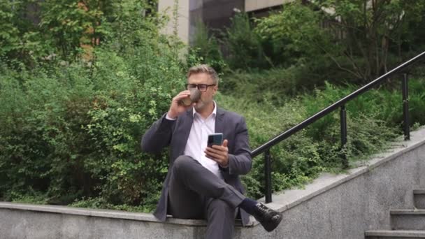 笑顔のビジネスマンはコーヒーを飲んで外でスマートフォンを使用しながら休憩します ビジネス コミュニケーション 技術コンセプト スローモーション — ストック動画