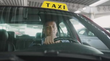 Afrikalı Amerikalı taksi şoförü araba kullanıyor ve elini direksiyonda tutuyor. Sarı taksi arabası tabelası. İnsanlar, iş, hizmet kavramı. Yavaş çekim