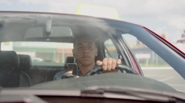 Afrikalı Amerikalı taksi şoförü araba sürerken akıllı telefondan mesaj okuyor. Sarı taksi arabası tabelası. İnsanlar, iş, hizmet kavramı. Yavaş çekim