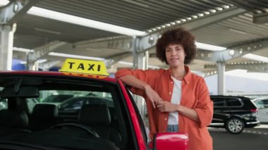 Güzel Afrika kökenli Amerikalı taksi şoförü park yerinde dikilirken başparmağını kaldırıyor. Sarı taksi arabası tabelası. İnsanlar, iş, hizmet kavramı. Yavaş çekim