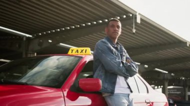 Afrikalı Amerikalı taksi şoförü kollarını kavuşturarak kırmızı arabaya yaslanıyor. Sarı taksi arabası tabelası. İnsanlar, iş, hizmet kavramı. Yavaş çekim