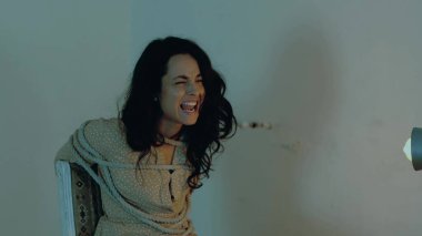 Erkek soyguncu masaya yumruğunu vuruyor ve kadını bıçakla tehdit ediyor. Kadın rehine sandalyeye bağlanmış ve çığlık atıyor. Adam kaçırma, suç, şiddet kavramı. Yavaş çekim