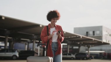 Dışarıda taksiyi beklerken telefonda yazan gülümseyen Afrikalı Amerikalı kadın. İnsanlar, yaşam tarzı, seyahat konsepti. Yavaş çekim