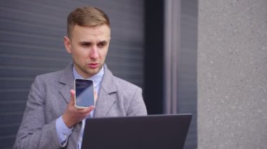 Genç adam dışarıda akıllı telefonla konuşurken dizüstü bilgisayarla çalışıyor. İş, iş, teknoloji konsepti. Yavaş çekim