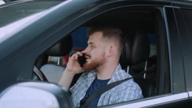 Genç adam akıllı telefon kullanırken sürücü koltuğunda oturuyor ve konuşuyor. Ulaşım, teknoloji, seyahat konsepti. Yavaş çekim
