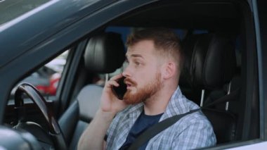 Arabada emniyet kemeri takan, cep telefonuyla konuşan beyaz bir adam. Ulaşım, teknoloji, seyahat konsepti. Yavaş çekim