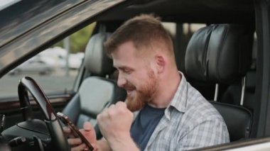 Arabada sürücü koltuğunda otururken mesajları okuyan gülümseyen genç adam. Ulaşım, teknoloji, seyahat konsepti. Yavaş çekim