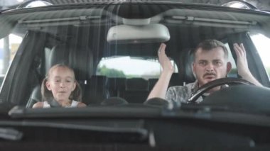 Baba küfrediyor ve araba kullanıyor, kızı yolcu koltuğunda şaşırmış. Ulaşım, güvenlik, aile kavramı. Yavaş çekim